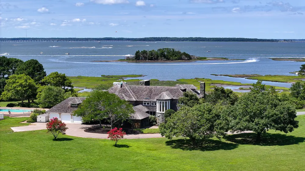 The house among old trees, with the bay and a small island behind it