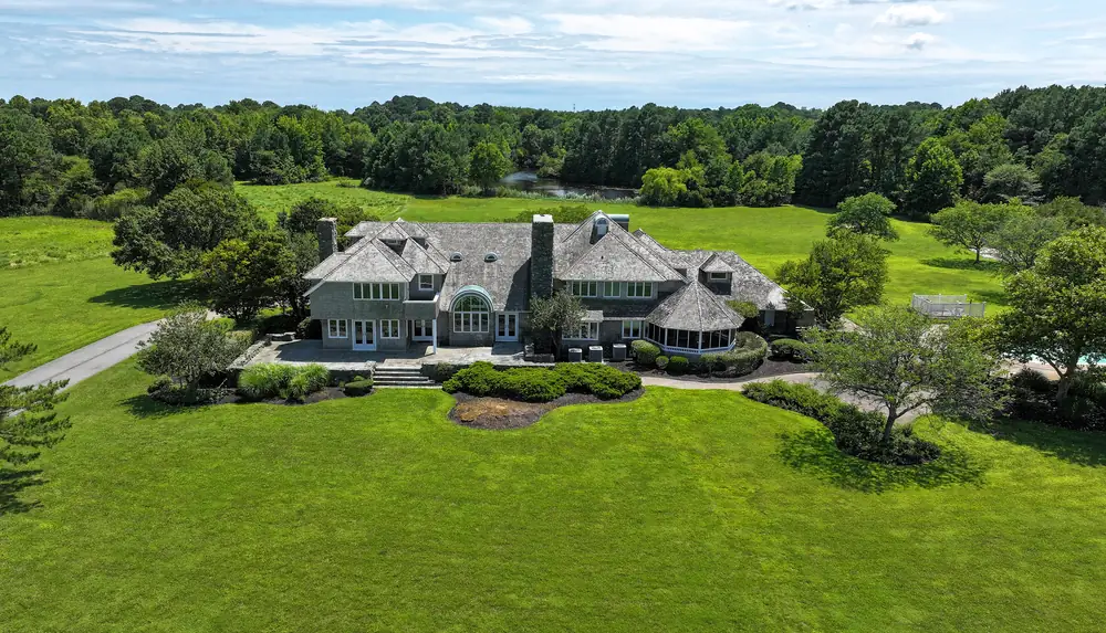 The bay side of the house: shingled gables, two stone chimneys, an arched window and a round screened porch, set on a wide lawn