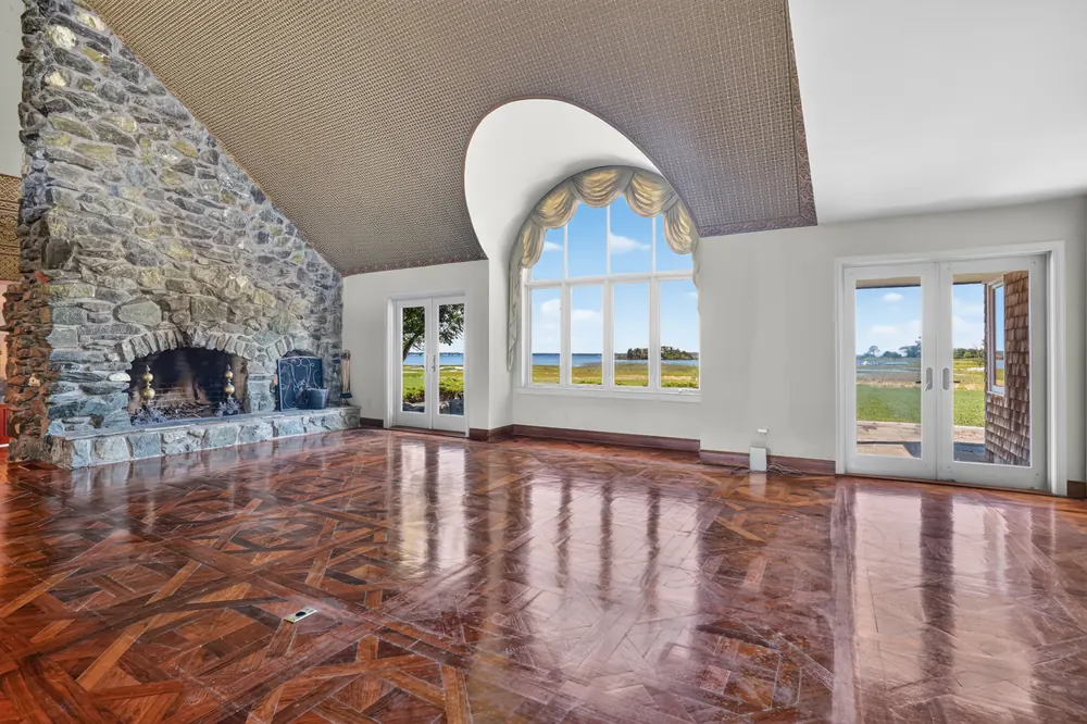 The great room: a floor-to-ceiling stone fireplace, an arched window and French doors, over a patterned wood floor