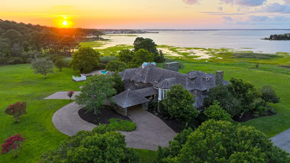 Aerial view at sunset of the shingled estate at 12903 Windy Drive, with its circular drive, the lawn and Isle of Wight Bay beyond