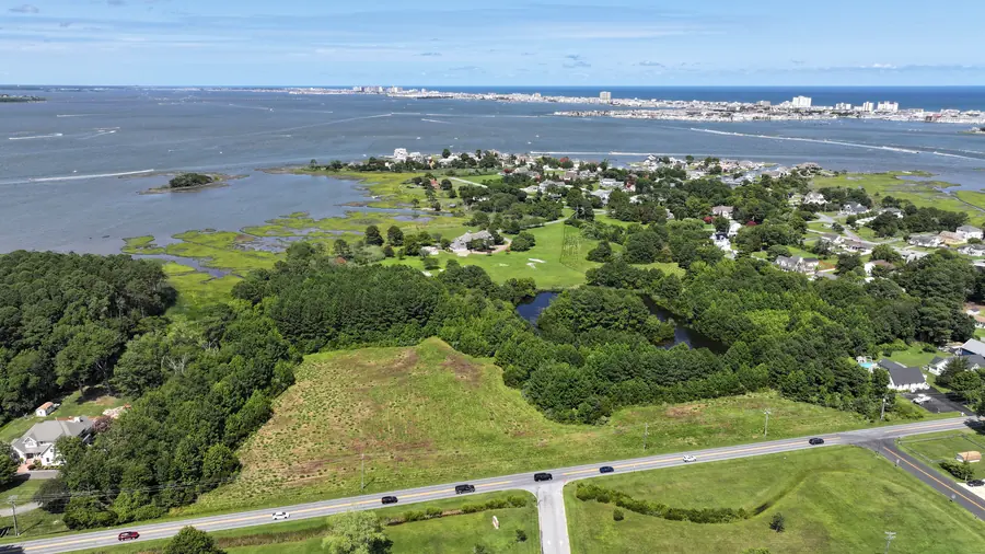 Aerial view of an open field along the road, with trees, a pond and the bay beyond