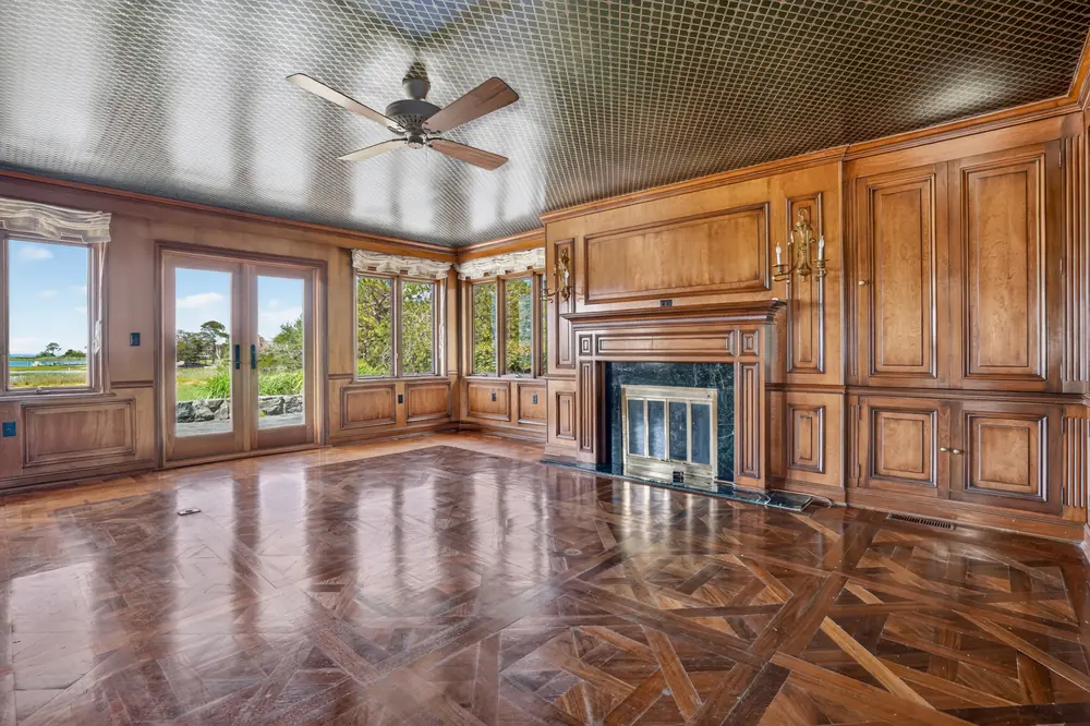 The walnut-paneled library with a marble fireplace and French doors to the lawn